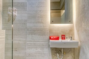 A bathroom with a white sink, a mirror, and a glass shower enclosure. - RedDoorz Plus near Gandaria City Mall 2 (Jakarta)