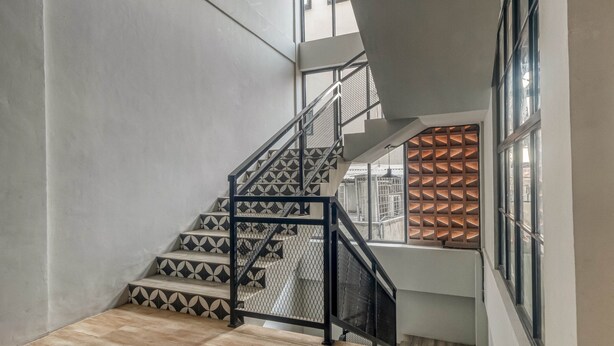 A staircase with geometric patterned steps and a metal railing, leading to a landing with a patterned wall and a window with a grid-like design. - RedDoorz Plus near Gandaria City Mall 2 (Jakarta)