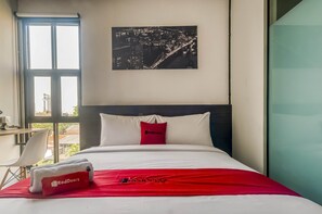 A hotel room with a bed, a window, a desk, and a cityscape view. - RedDoorz Plus near Gandaria City Mall 2 (Jakarta)