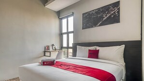 A hotel room with a large bed, a red throw blanket, a red pillow, a nightstand with a lamp, and a cityscape painting on the wall. - RedDoorz Plus near Gandaria City Mall 2 (Jakarta)