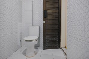 Et lille, hvidt toilet i et badeværelse med hvide, mønstrede fliser og en trådør.