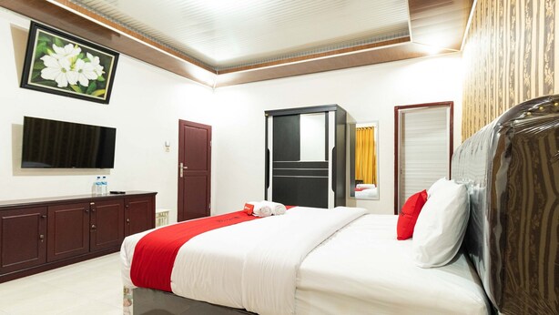A hotel room with a bed, a TV, a wardrobe, and a mirror. - RedDoorz Plus near Universitas Methodist Medan (Medan)