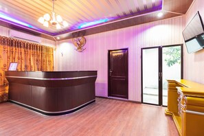 A reception area with a curved reception desk, a closed door, and a television mounted on the wall. - RedDoorz Plus near Universitas Methodist Medan (Medan)