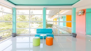 Une pièce lumineuse et moderne, avec un canapé de couleur turquoise, une petite table ronde et deux tabourets. De grandes fenêtres offrent une vue sur la verdure environnante.
