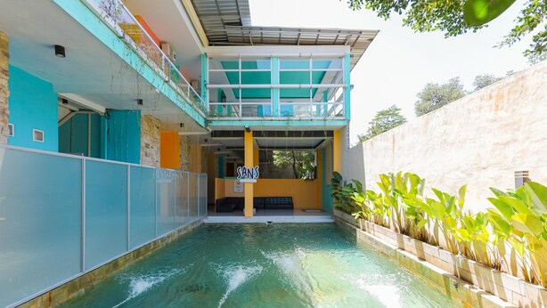 Une piscine avec un panneau indiquant « SANS » au centre, entourée d’un bâtiment doté d’un balcon et d’un mur en pierre.