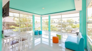 Une pièce lumineuse et moderne, dotée de grandes fenêtres, d’une table blanche avec des chaises et de sièges aux couleurs vives.