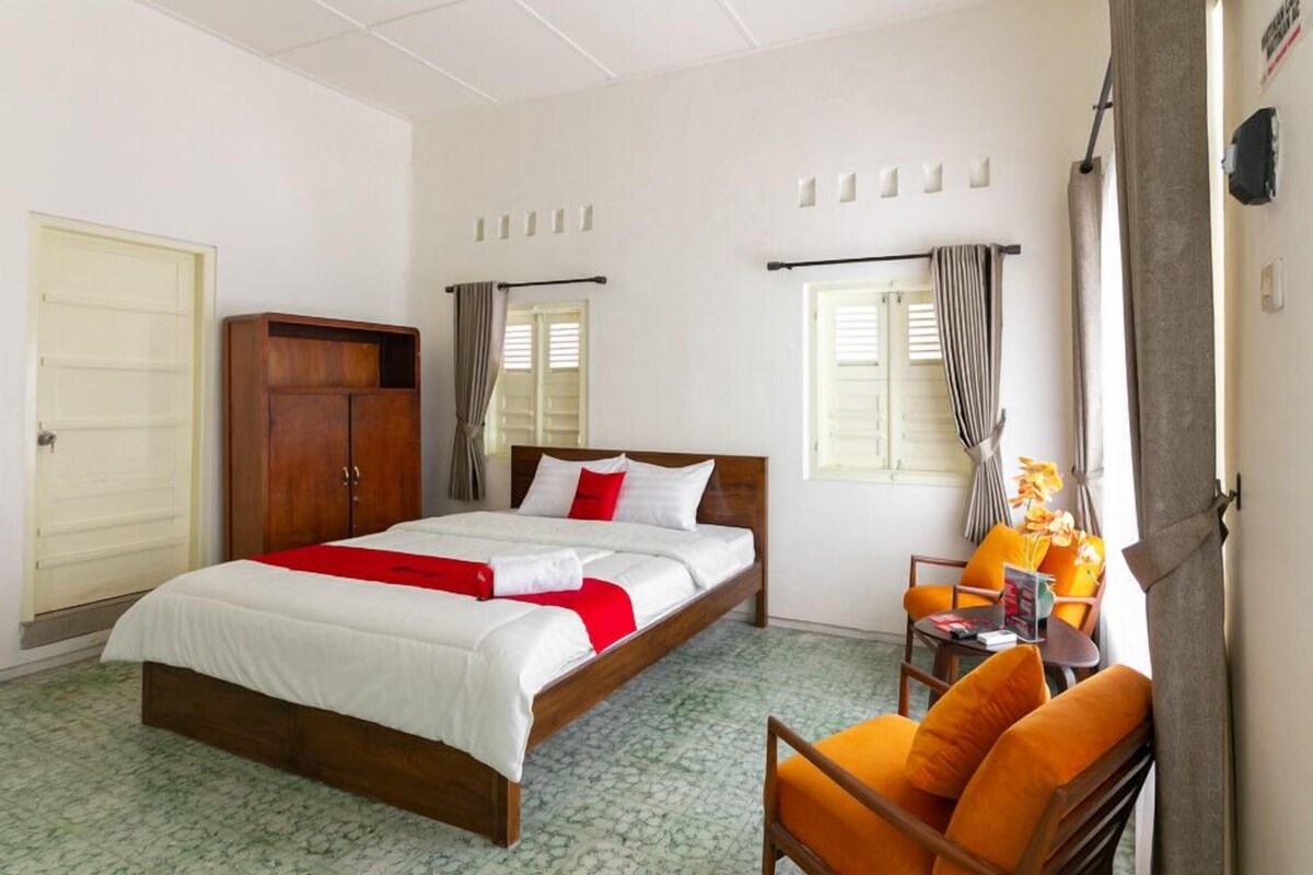 Une chambre d’hôtel avec un lit, une armoire en bois, une petite table avec une chaise et une fenêtre avec des rideaux.