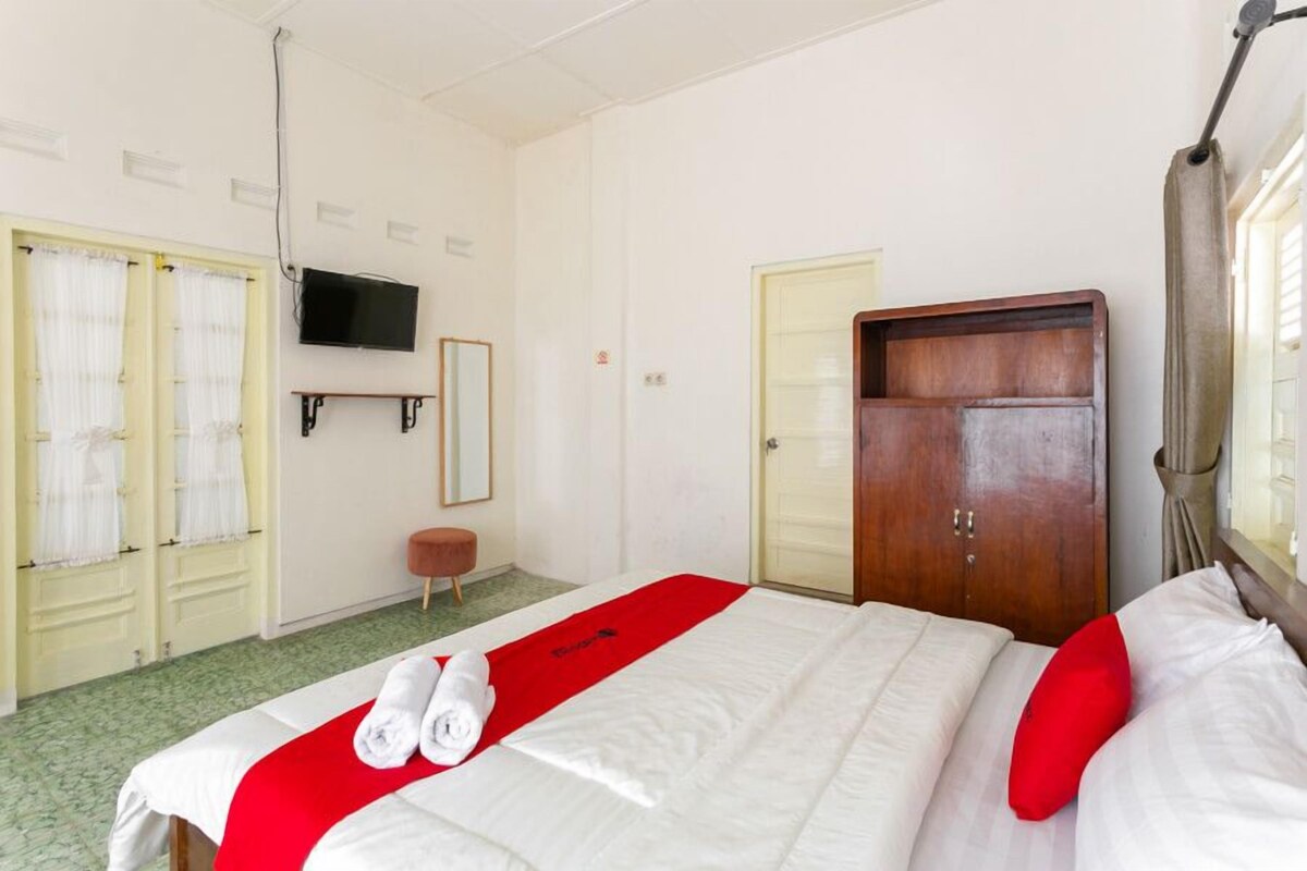 Une chambre d’hôtel avec un lit, un téléviseur fixé au mur, une armoire en bois et un petit tabouret.