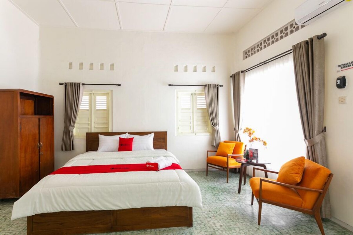 A hotel room with a bed, a wooden wardrobe, a small table, two chairs, and a window with curtains.