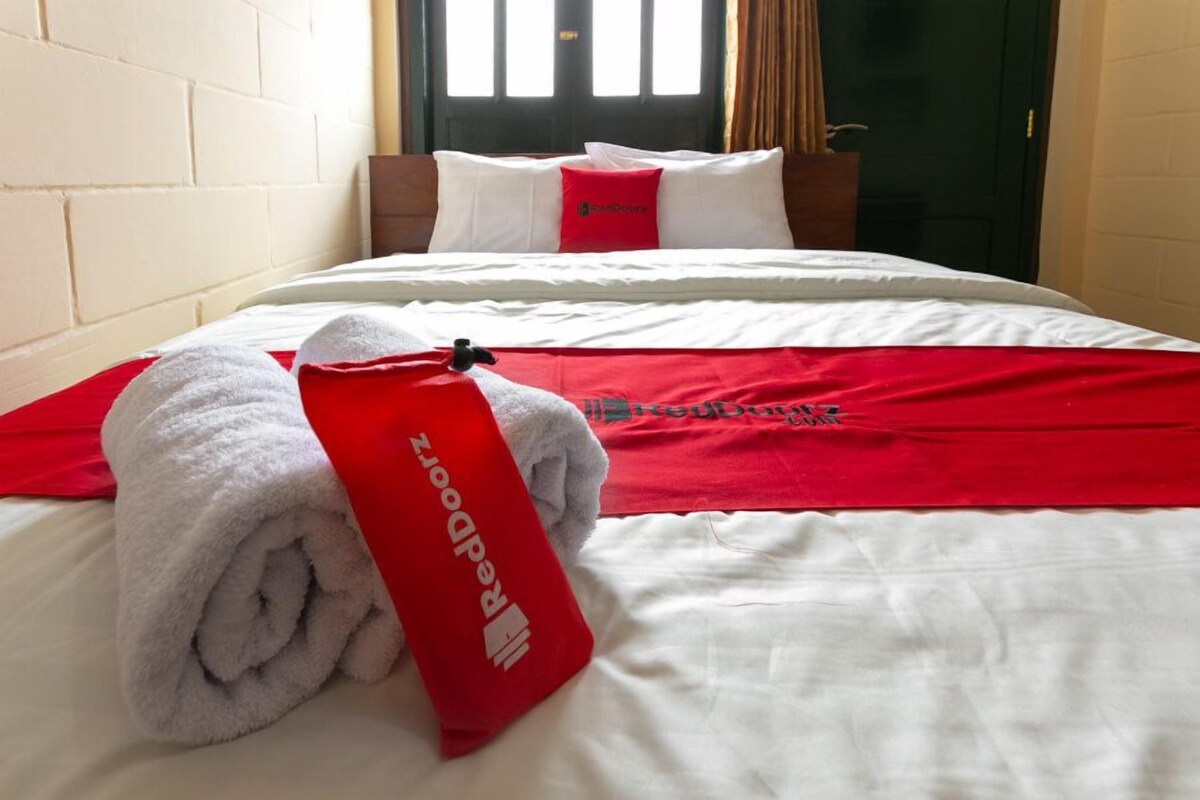 Un lit bien fait, avec une serviette rouge et une autre serviette rouge ornée du logo « ReedDoors ».