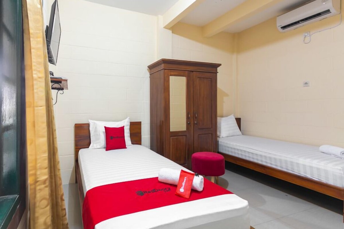 A hotel room with a bed, a wooden wardrobe, a TV, and an air conditioning unit.