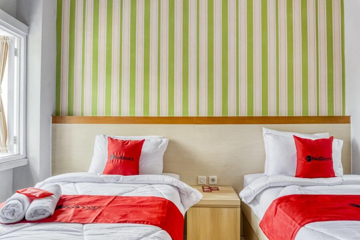 Una habitación de hotel con dos camas, cada una con ropa de cama roja y blanca, una pared verde y blanca a rayas y un cabecero de madera.