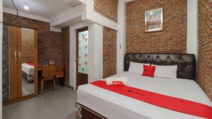 A hotel room with a brick wall, a bed with a red and white bedspread, a wooden desk, and a chair. - RedDoorz Syariah near Jalan Asahan Pematang Siantar (Pematangsiantar)