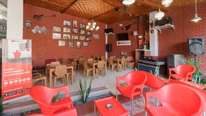 A restaurant with wooden tables and chairs, a brick wall with pictures, and a RedDoorz sign. - RedDoorz Syariah near Jalan Asahan Pematang Siantar (Pematangsiantar)