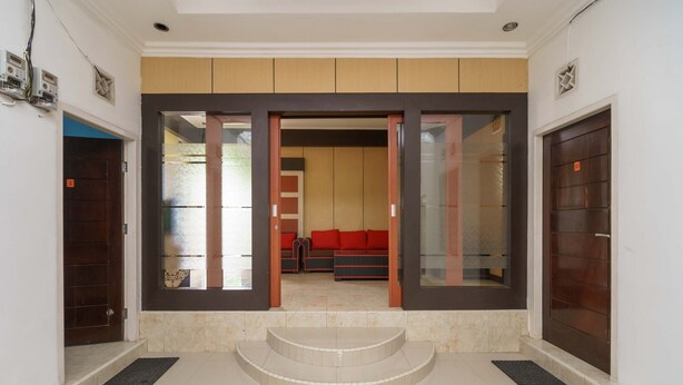 Un vestíbulo de hotel con diseño moderno, que cuenta con un amplio acceso por puerta de vidrio, una zona de estar con sofás rojos y un suelo de mármol.