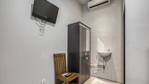 Une petite salle de bain avec une chaise en bois, un meuble, un lavabo et un téléviseur fixé au mur.