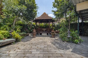 Ein Gazebo mit Ziegeldach, umgeben von üppiger Vegetation und Pflastersteinen.