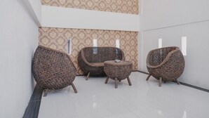 A modern interior with wicker furniture, including a chair and a small table, against a patterned wall. - RedDoorz Apartment @ Batam Centre 3 (Batam)
