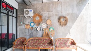 A room with a concrete wall, a fan, and a variety of woven baskets and mats. There are three wooden sofas with patterned upholstery. - RedDoorz Syariah @ Winong Nganjuk (Nganjuk)
