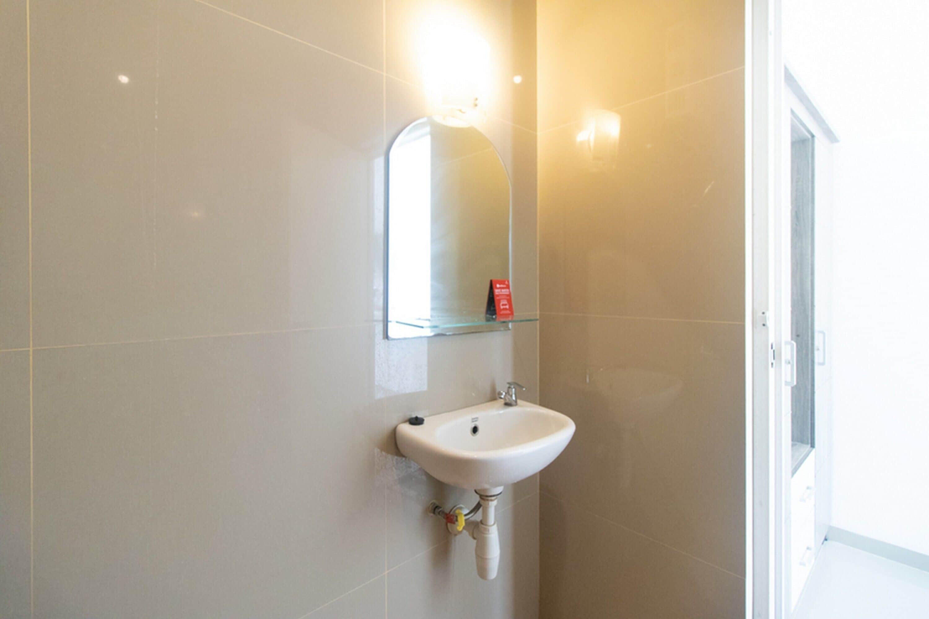 Une salle de bain avec un lavabo blanc, un miroir et une étagère en verre au-dessus du lavabo.