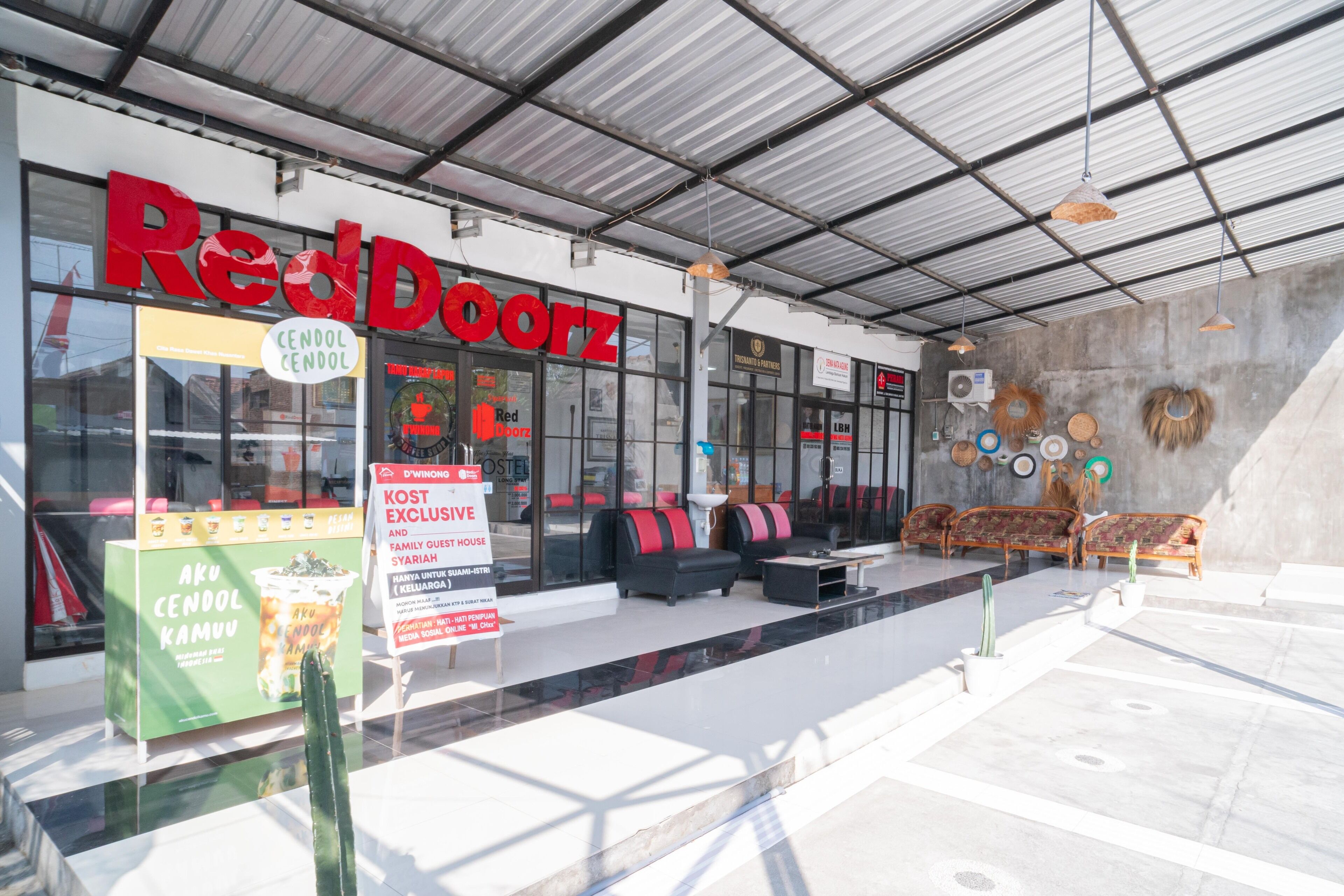A RedDoorz store with a modern design, featuring a glass facade, outdoor seating area, and a sign advertising a special offer.