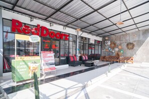 Una tienda RedDoorz con diseño moderno, que cuenta con fachada de vidrio, zona de estar al aire libre y un cartel que anuncia una oferta especial.