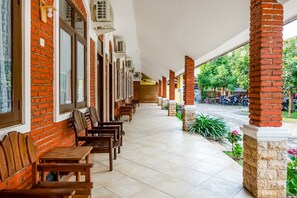 A covered outdoor seating area with brick walls and tiled flooring, featuring rows of wooden tables and chairs. - RedDoorz Syariah near Gor Ken Arok (Malang)