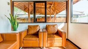 A room with a large window, a brown leather sofa, and a potted plant. - RedDoorz Syariah near Gor Ken Arok (Malang)