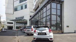 A parking lot with several cars parked in front of a building with large windows and a covered entrance. - RedDoorz Apartment near Grand City Mall (Surabaya)