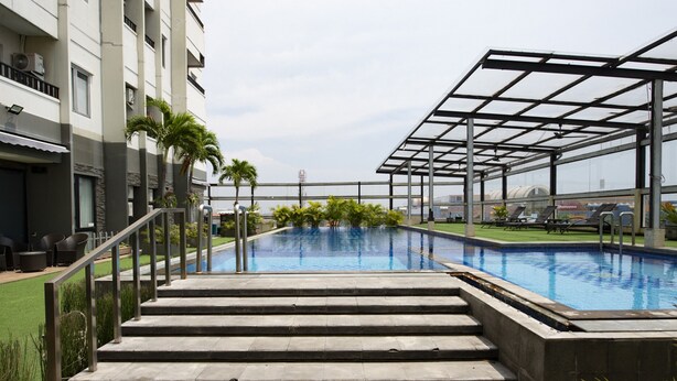 A swimming pool with steps leading up to it, surrounded by palm trees and a covered area with lounge chairs. - RedDoorz Apartment near Grand City Mall (Surabaya)