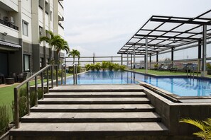 A swimming pool with steps leading up to it, surrounded by palm trees and a covered area with lounge chairs.