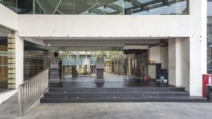 A modern building entrance with a glass facade, a central statue, and a staircase leading to an upper level. - RedDoorz Apartment near Grand City Mall (Surabaya)