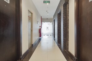Un couloir d’hôtel avec un sol carrelé, une porte portant l’inscription « SORTIE », et un mur orné d’un motif sur le côté droit.