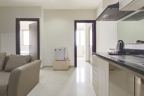 Eine moderne Küche mit Einbauherd, Kaffeemaschine und Kühlschrank. Im Wohnbereich befindet sich ein beiges Sofa und eine Tür zu einem weiteren Raum.