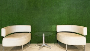 Two white leather armchairs and a glass table with metal legs, positioned against a green wall. - RedDoorz Apartment near Grand City Mall (Surabaya)