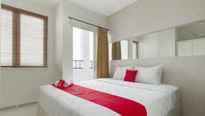 A hotel room with a large bed, a red throw, a white pillow, and a window with blinds. - RedDoorz Apartment near Grand City Mall (Surabaya)