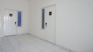 A hallway with two doors, each marked with a number. The floor is tiled, and the walls are plain white. - RedDoorz near Alun Alun Kaliwungu Kendal (Kaliwungu)