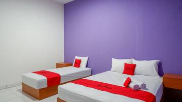 A hotel room with two single beds, each with a red and white bedspread, and a purple accent wall.