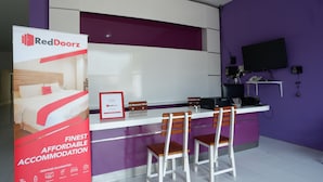 A RedDoorz reception desk with a purple wall, a flat-screen TV, and a signboard advertising the hotel's services. - RedDoorz near Alun Alun Kaliwungu Kendal (Kaliwungu)