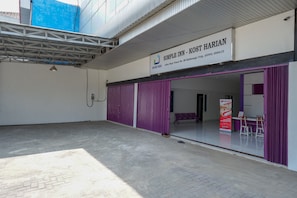 Un hotel llamado "Simple Inn - Kost Harian" con un letrero, un área exterior cubierta y una entrada morada.