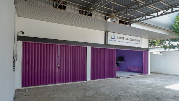 A hotel with closed purple doors, a sign above indicating it's the "Simple Inn - Kost Harian," and a concrete floor. - RedDoorz near Alun Alun Kaliwungu Kendal (Kaliwungu)