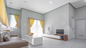 A modern living room with a sofa, a coffee table, a TV, and a staircase. - RedDoorz Resort Syariah @ Idelansia Homestay Ciater (Ciater)