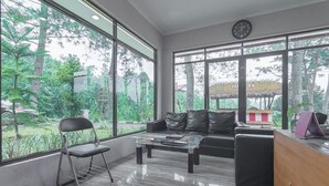 A modern living room with large windows, a sofa, a coffee table, and a chair. - RedDoorz Resort Syariah @ Idelansia Homestay Ciater (Ciater)