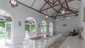 A spacious dining area with a long wooden table, white chairs, and large windows allowing natural light. - RedDoorz Resort Syariah @ Idelansia Homestay Ciater (Ciater)