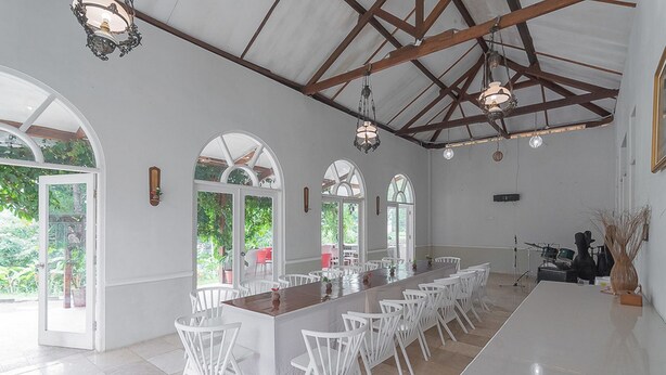A spacious dining area with a long wooden table, white chairs, and large windows allowing natural light. - RedDoorz Resort Syariah @ Idelansia Homestay Ciater (Ciater)
