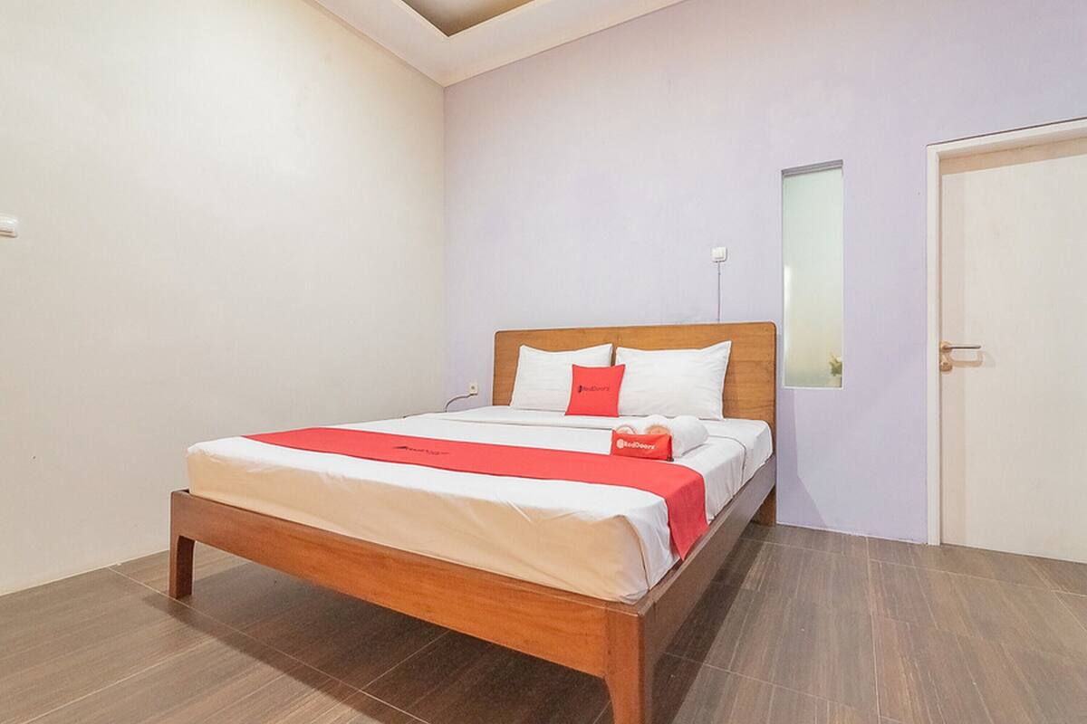 A neatly made bed with a wooden frame, white bedding, and a red accent pillow.