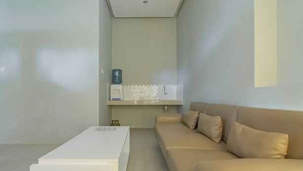 A modern living room with a beige sofa, a white coffee table, and a built-in shelf with a water dispenser. - RedDoorz Resort Syariah @ Idelansia Homestay Ciater (Ciater)