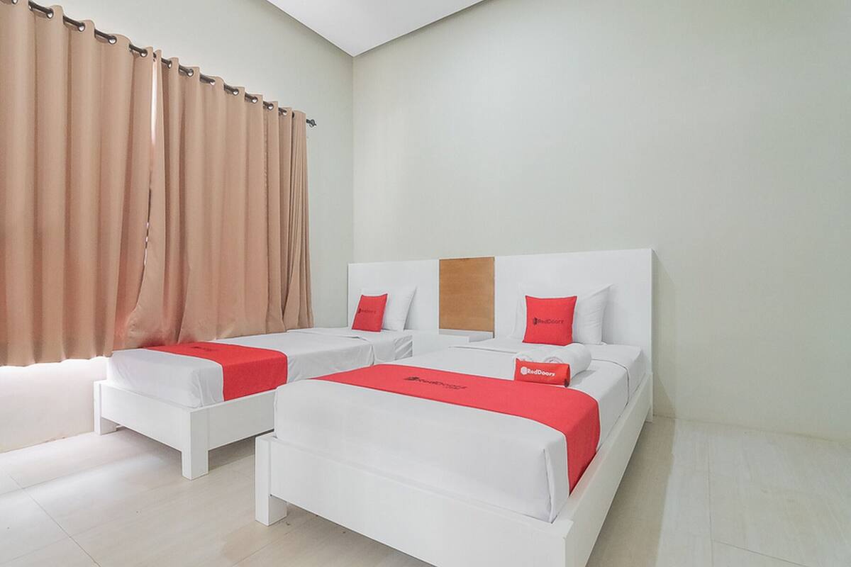 A hotel room with two single beds, a large bed, and a window with curtains.