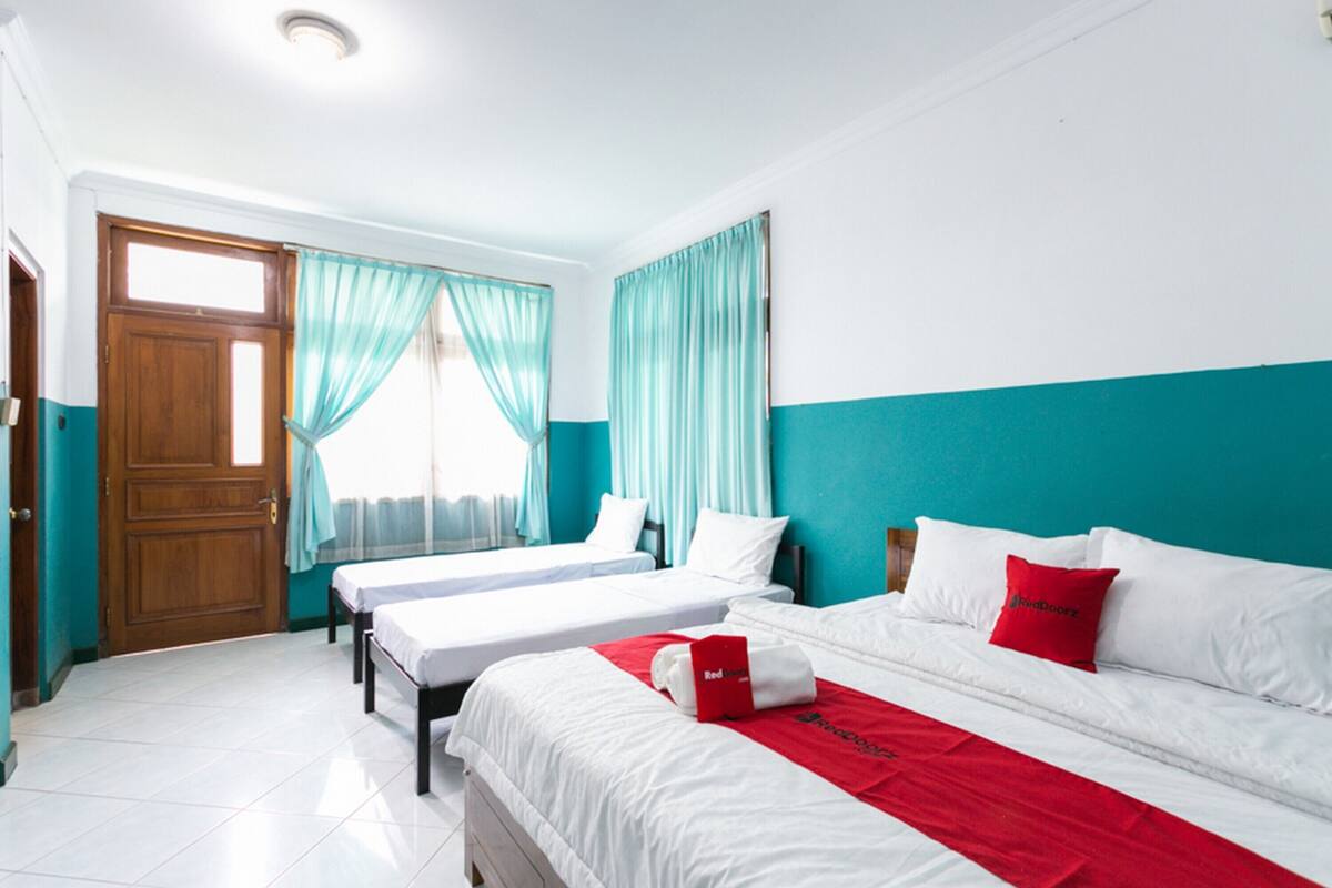Une chambre d’hôtel avec deux lits, des rideaux de couleur turquoise, des murs blancs et une porte en bois.