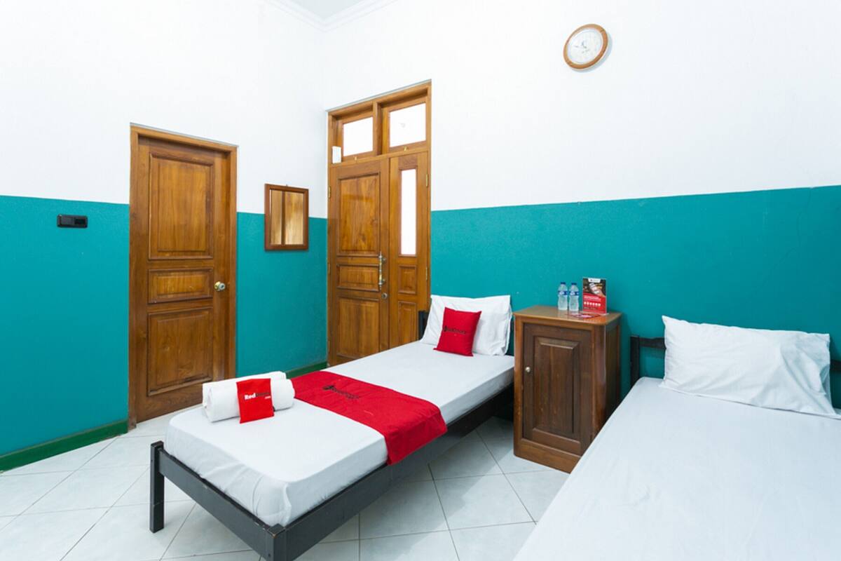 Une chambre d’hôtel avec deux lits, une armoire en bois et un petit meuble de rangement.